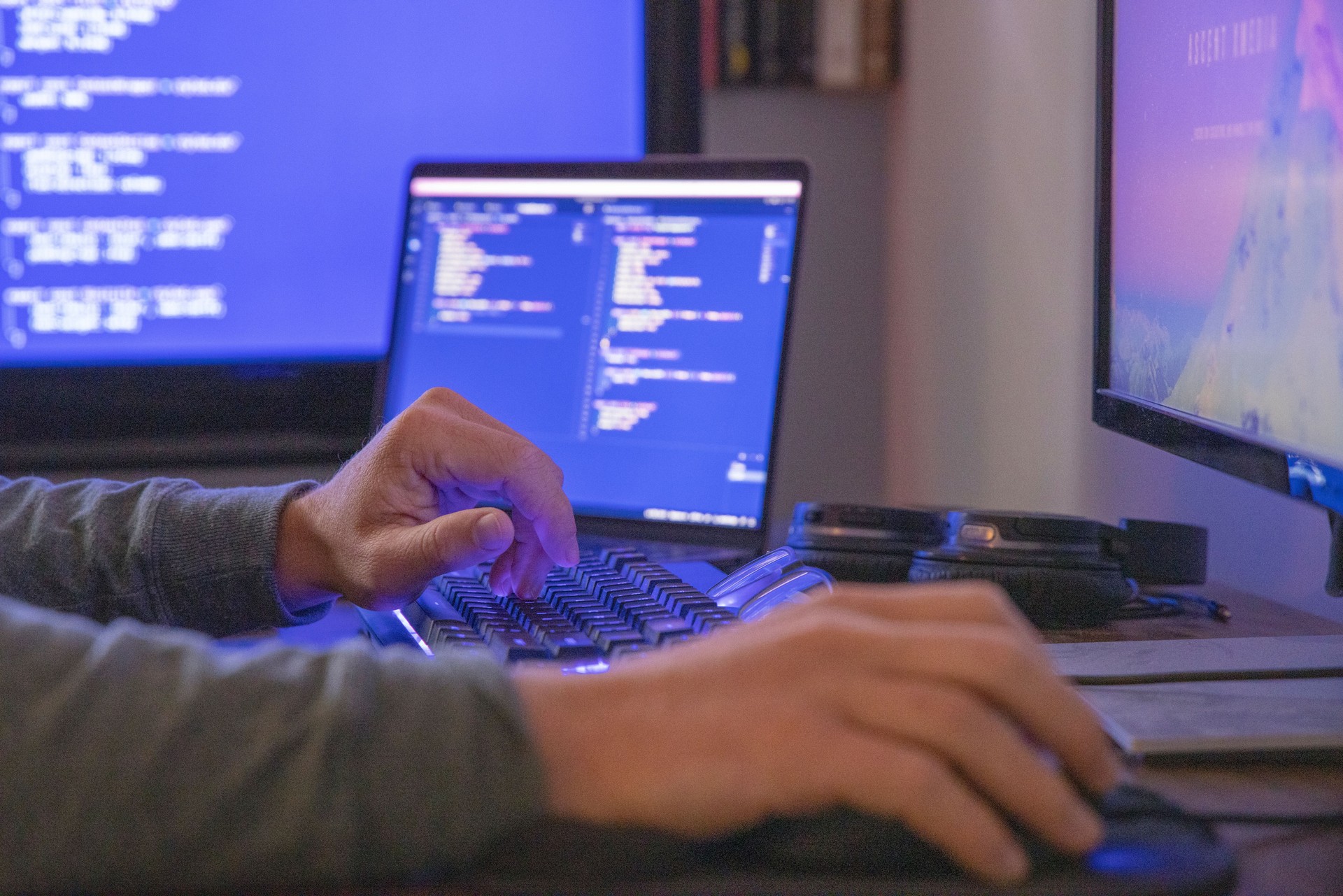 Young man uses multiple computers while coding, developing web site